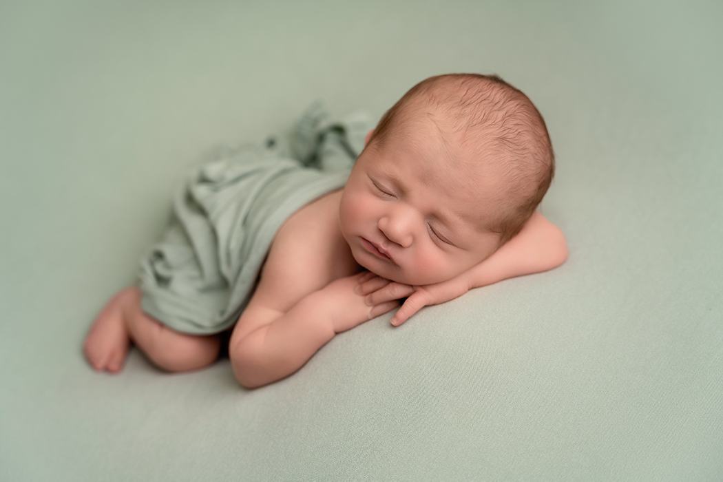 baby boy on sage green background in chin on hands pose